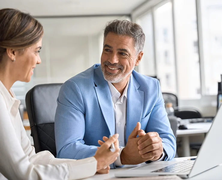 Manager and employee discuss project at desk with laptopManager and employee discuss project at desk with laptop